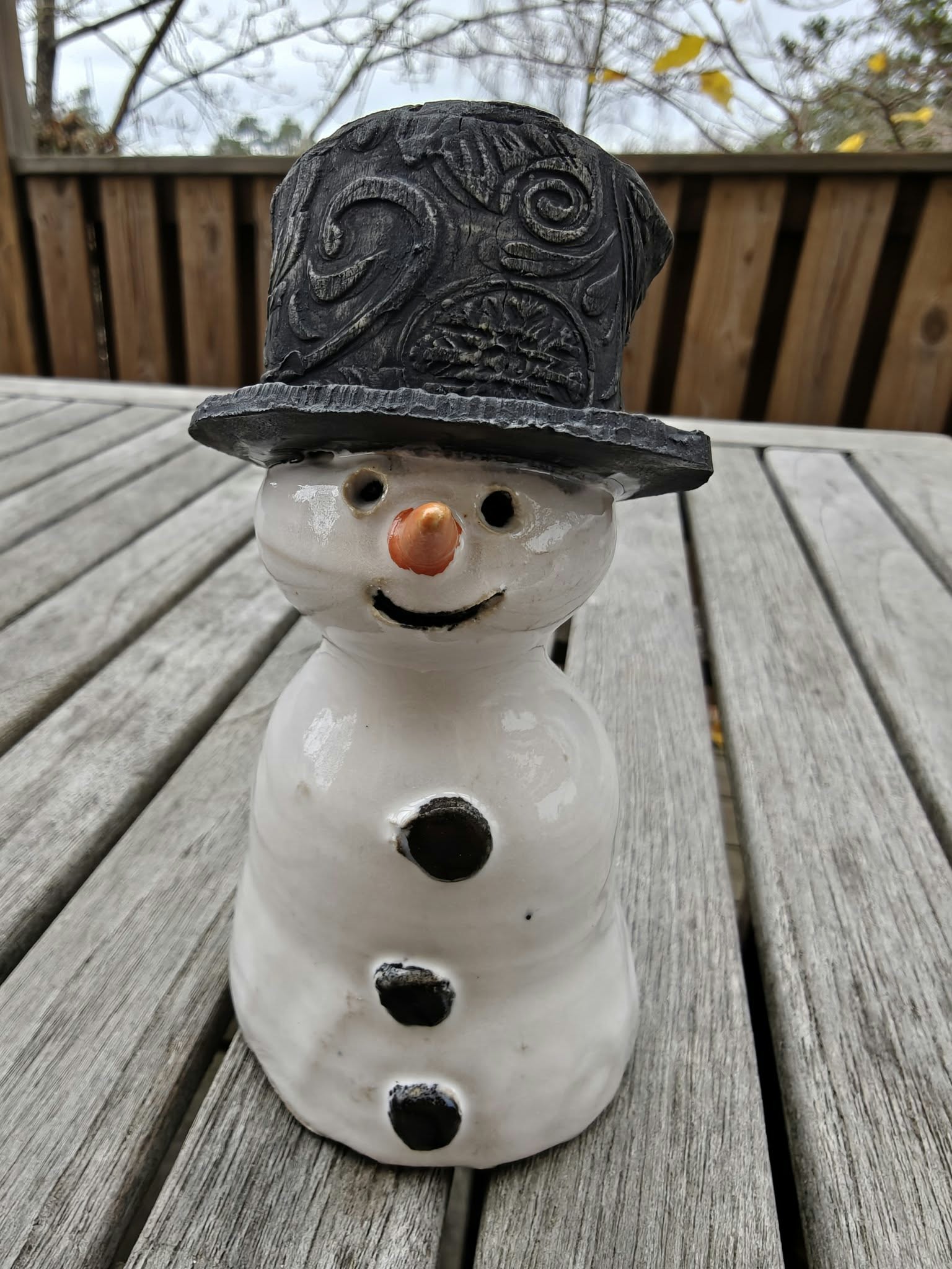 Snögubbe med svart hatt, morotsnäsa och knappar.
